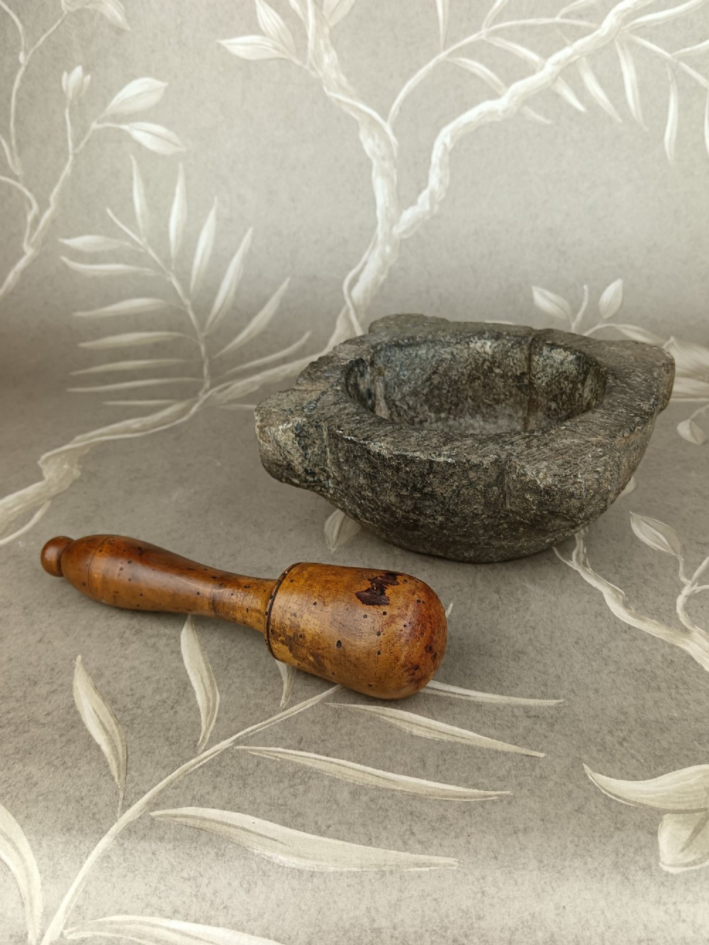 An antique hand-carved stone mortar featuring four corner lugs, shown with a turned fruitwood pestle. View IX