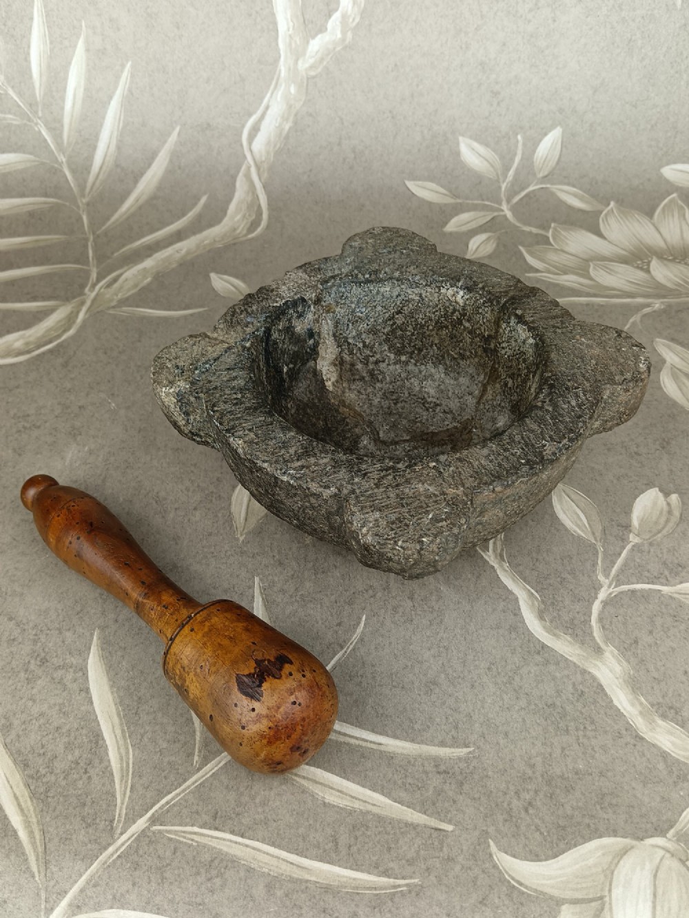 An antique hand-carved stone mortar featuring four corner lugs, shown with a turned fruitwood pestle. View X