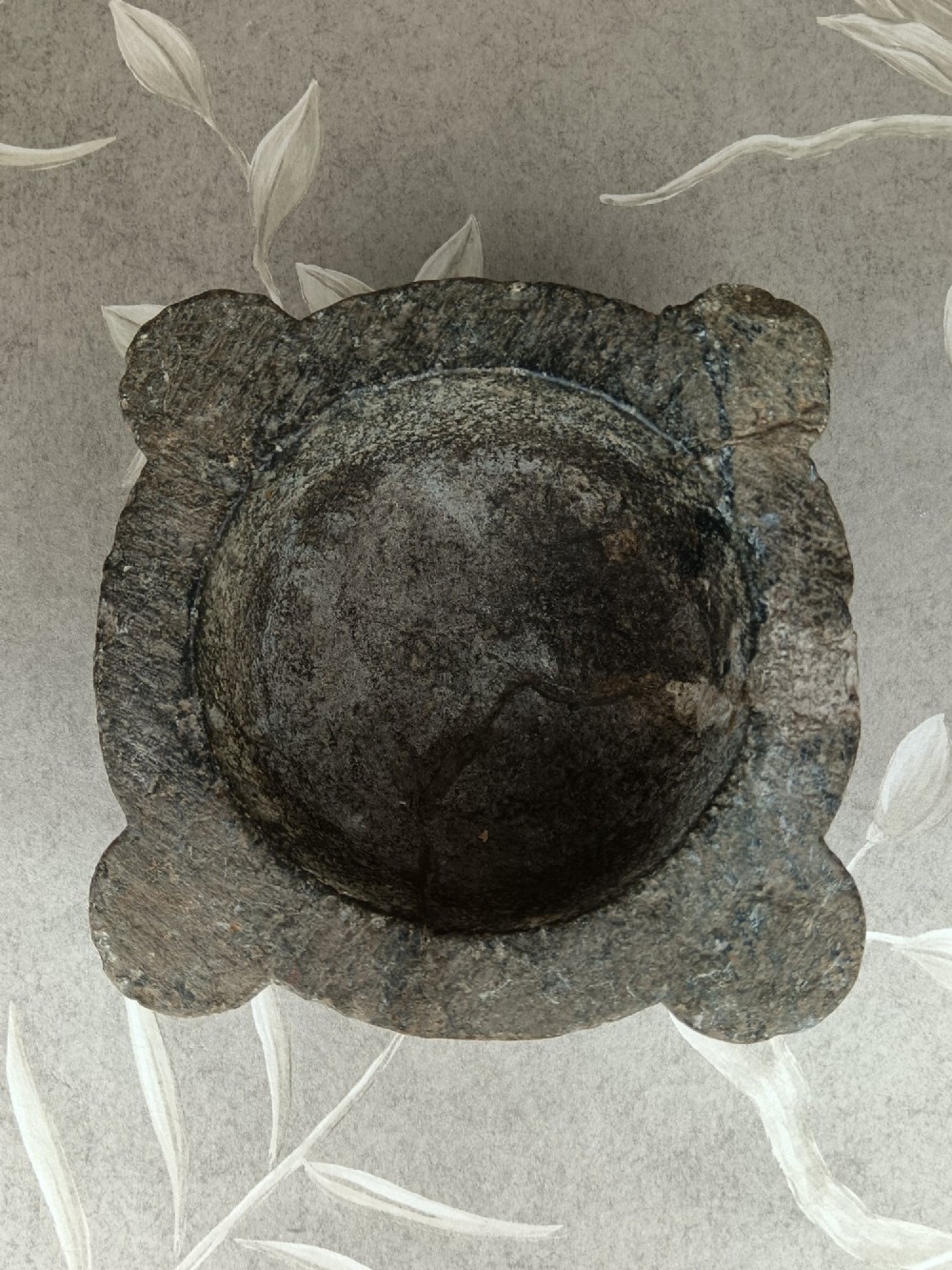An antique hand-carved stone mortar featuring four corner lugs, shown with a turned fruitwood pestle. View XII