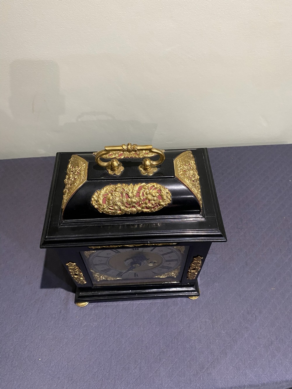 A late 17th-century black ebony bracket clock featuring decorative gilded brass mounts, a brass carrying handle, and a square glass face with a silvered chapter ring. View III