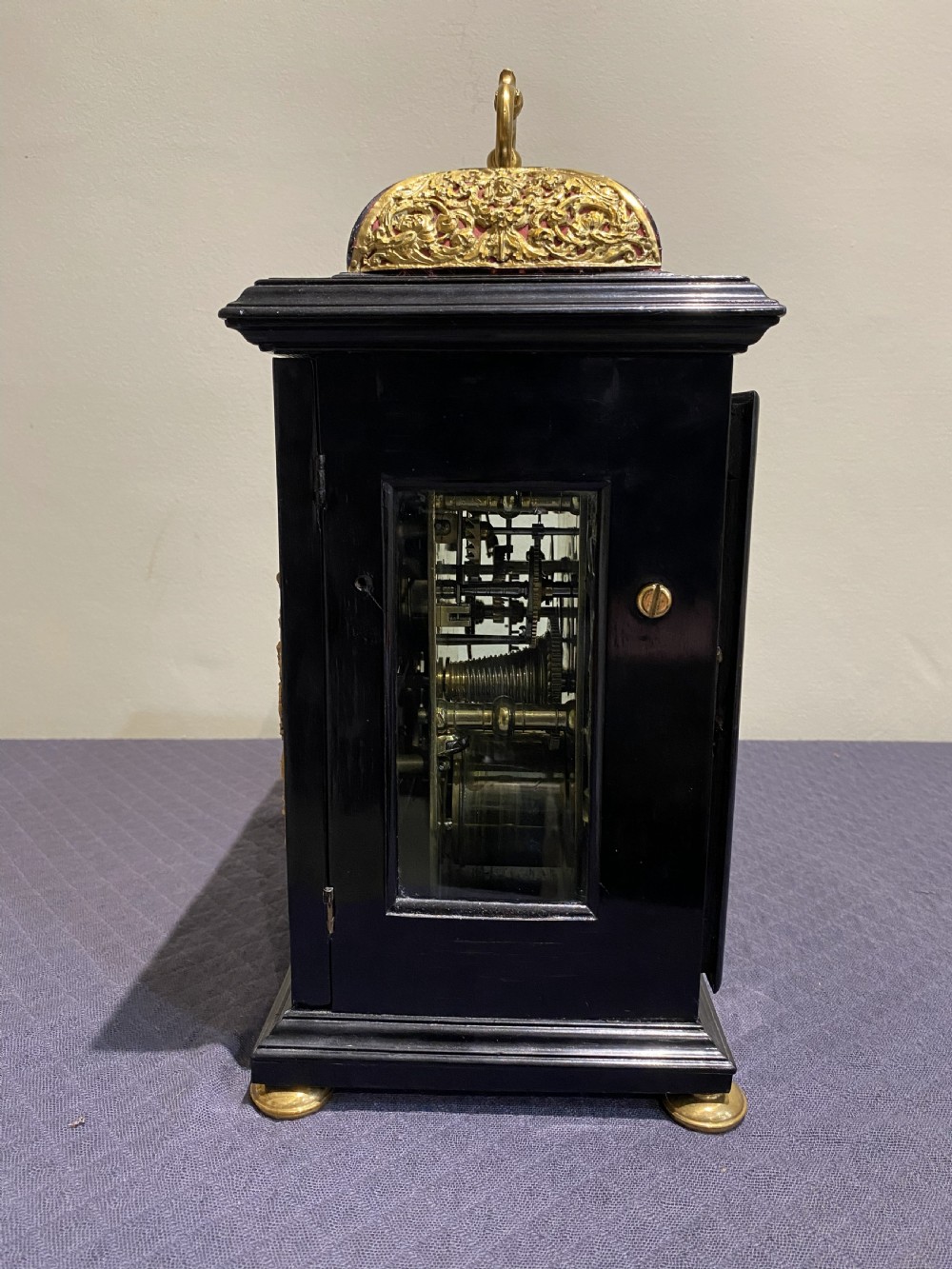 A late 17th-century black ebony bracket clock featuring decorative gilded brass mounts, a brass carrying handle, and a square glass face with a silvered chapter ring. View IV