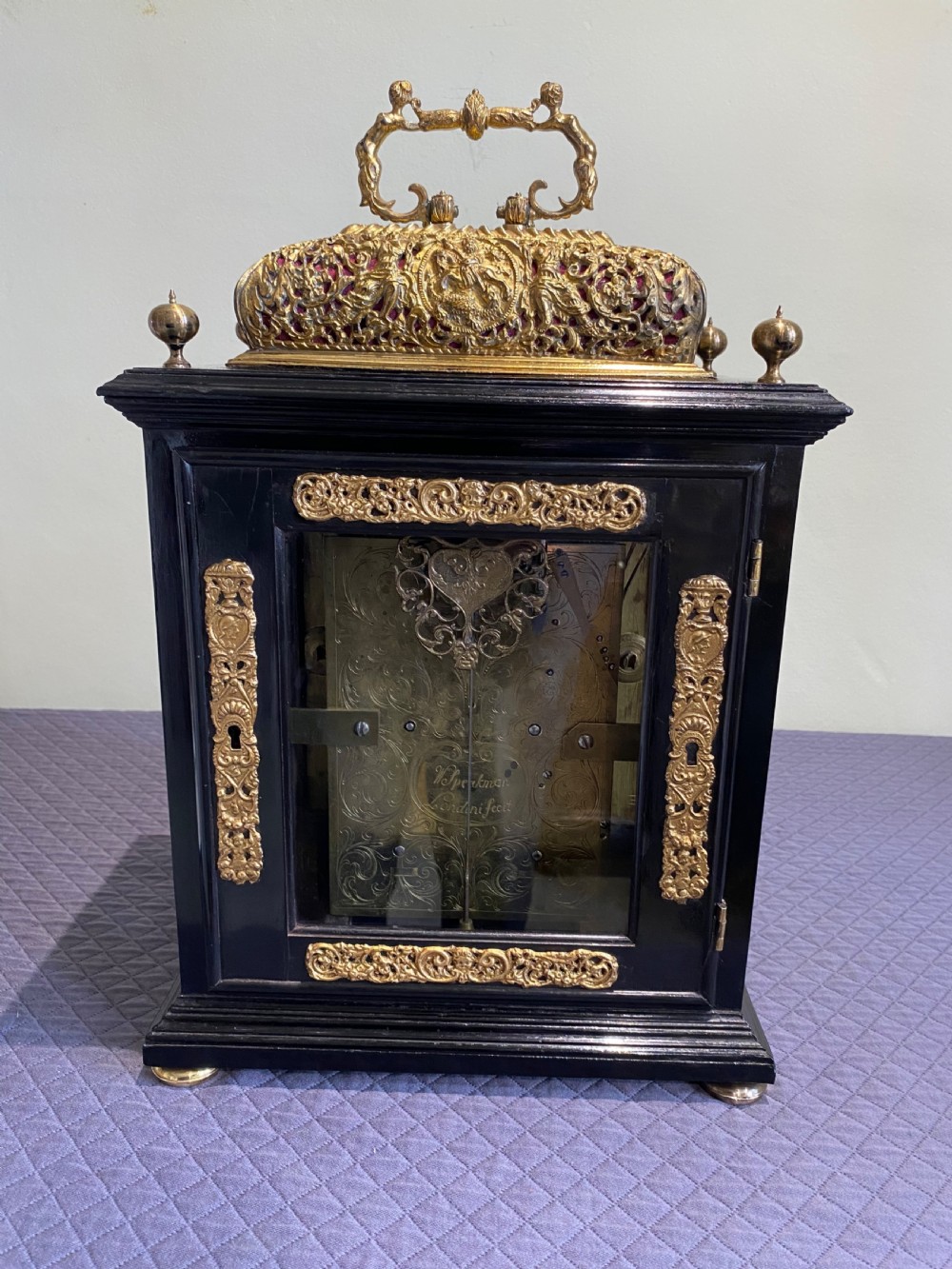 A late seventeenth-century William and Mary ebony table clock featuring an ornate gilded brass basket top with carrying handle and silvered chapter ring. View II