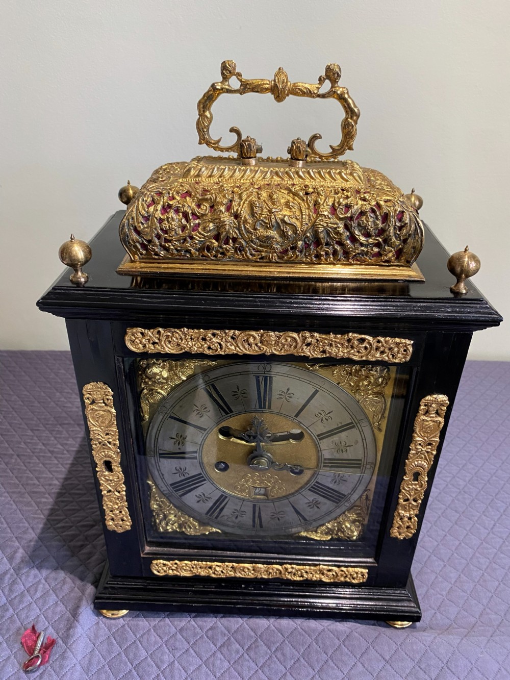 A late seventeenth-century William and Mary ebony table clock featuring an ornate gilded brass basket top with carrying handle and silvered chapter ring.