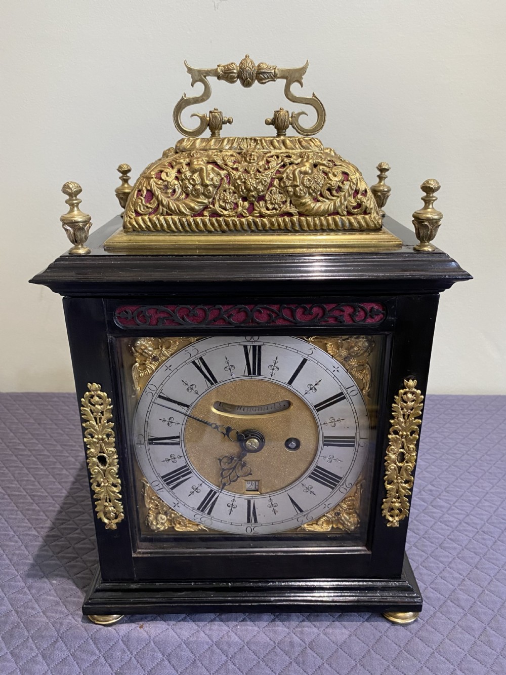 A late 17th-century ebony-veneered table clock with a pierced gilt-brass basket top, decorative finials, and a silvered roman numeral chapter ring.