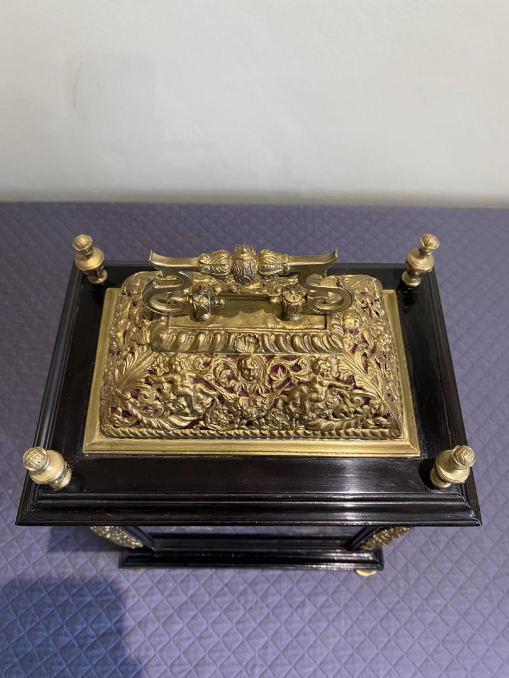 A late 17th-century ebony-veneered table clock with a pierced gilt-brass basket top, decorative finials, and a silvered roman numeral chapter ring. View IV