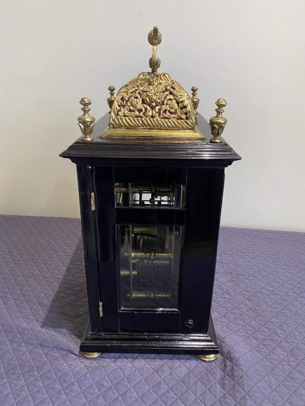 A late 17th-century ebony-veneered table clock with a pierced gilt-brass basket top, decorative finials, and a silvered roman numeral chapter ring. View VI