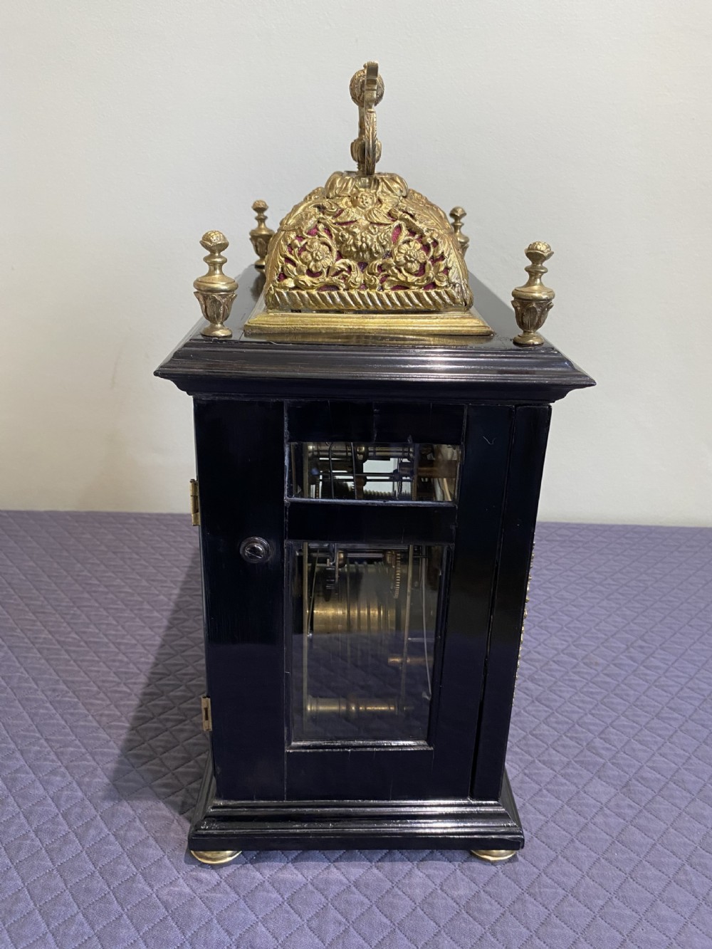 A late 17th-century ebony-veneered table clock with a pierced gilt-brass basket top, decorative finials, and a silvered roman numeral chapter ring. View VIII