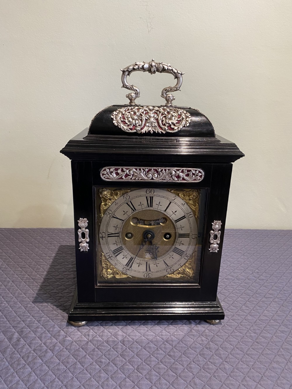A late 17th-century black ebony table clock featuring repousse silver mounts, an ornate carrying handle, and a brass dial with silvered chapter ring.