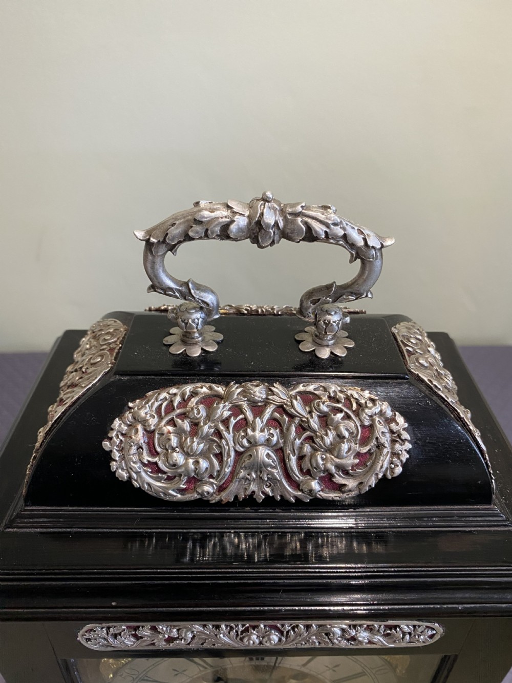 A late 17th-century black ebony table clock featuring repousse silver mounts, an ornate carrying handle, and a brass dial with silvered chapter ring. View IX