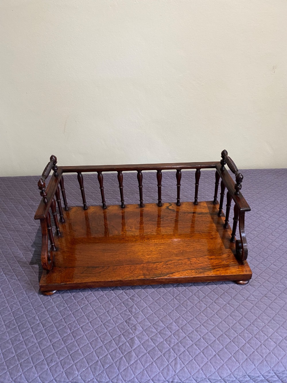 A 19th-century Regency rosewood tabletop book rack featuring a turned spindle back gallery and carved side handles. View V
