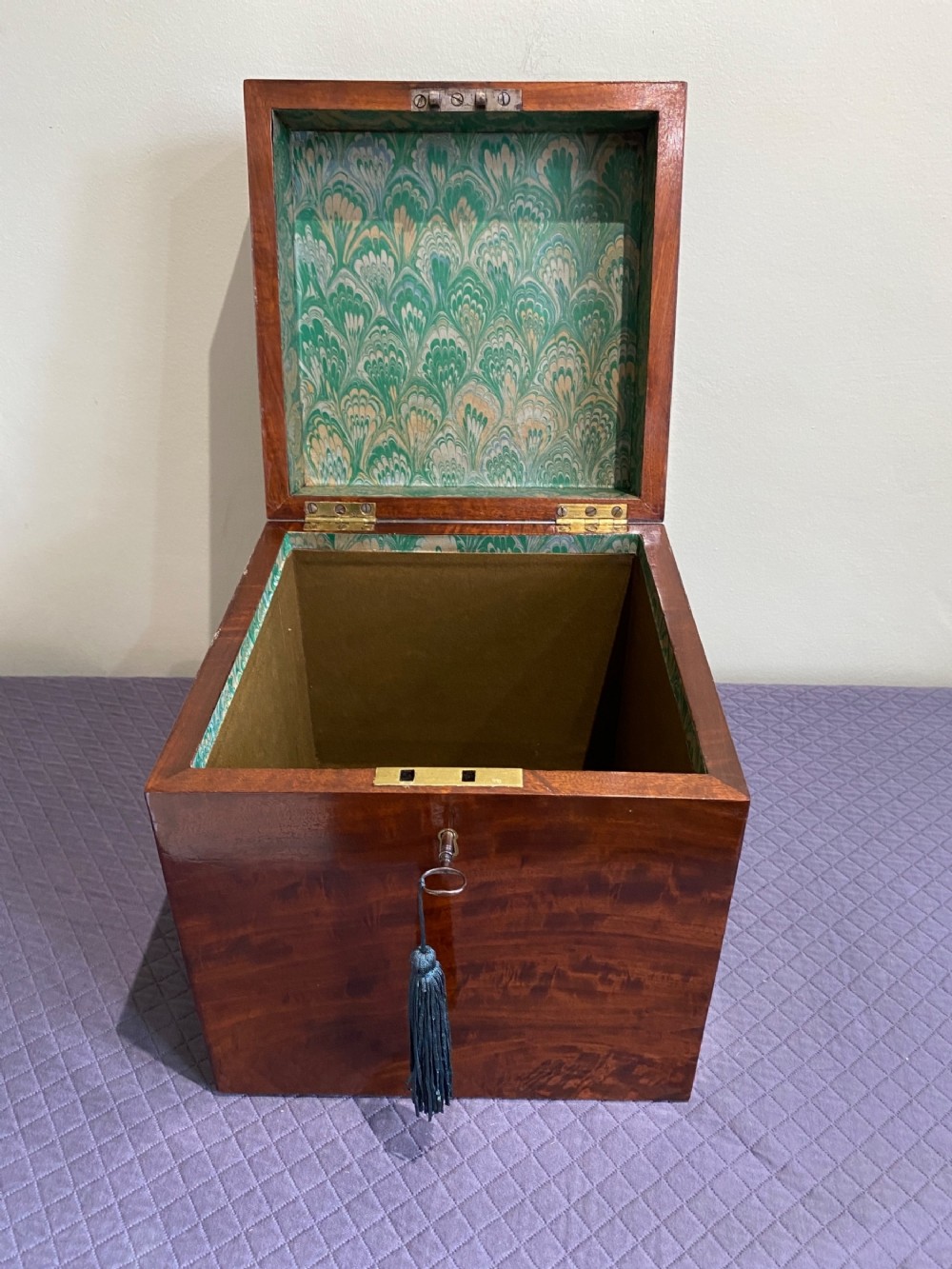 An open Georgian mahogany box featuring a polished timber grain exterior, a brass lock with key, and an interior lined with green marbled paper.