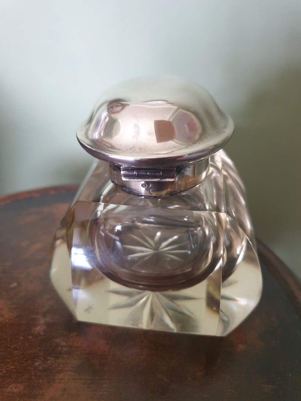 A heavy clear cut-glass inkwell featuring a starburst base design and a polished hinged silver lid with hallmarks.