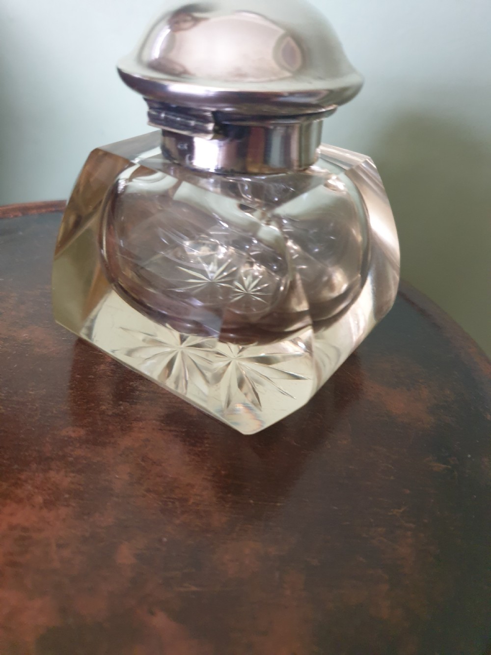 A heavy clear cut-glass inkwell featuring a starburst base design and a polished hinged silver lid with hallmarks. View IV