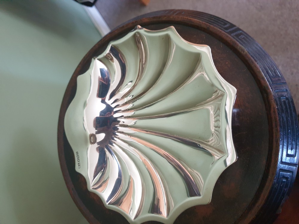 A polished sterling silver dish shaped like a scalloped sea shell with visible British hallmarks on the outer rim.