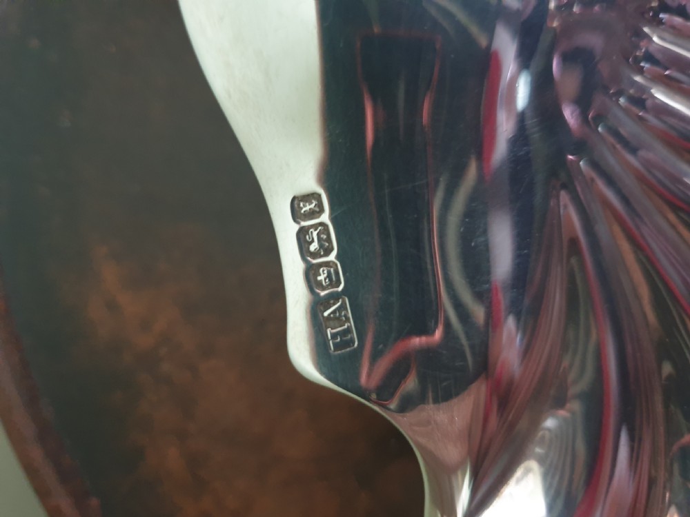 A polished sterling silver dish shaped like a scalloped sea shell with visible British hallmarks on the outer rim. View II