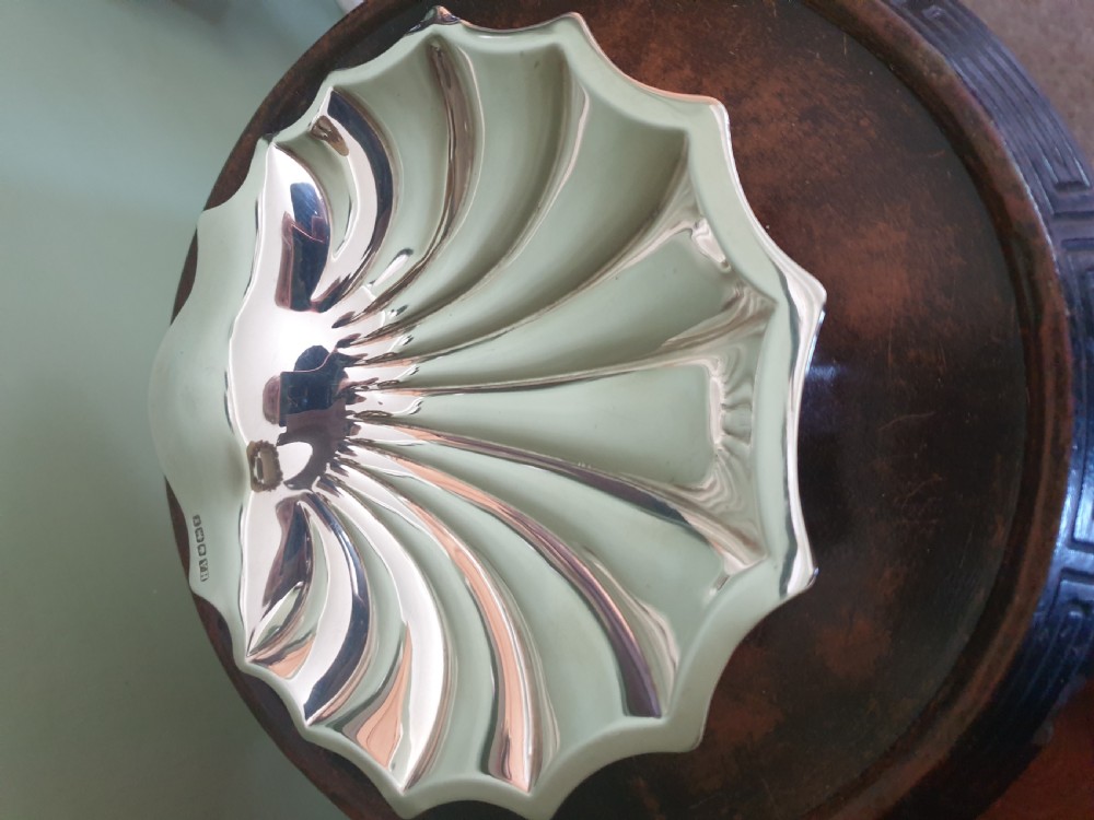 A polished sterling silver dish shaped like a scalloped sea shell with visible British hallmarks on the outer rim. View IV