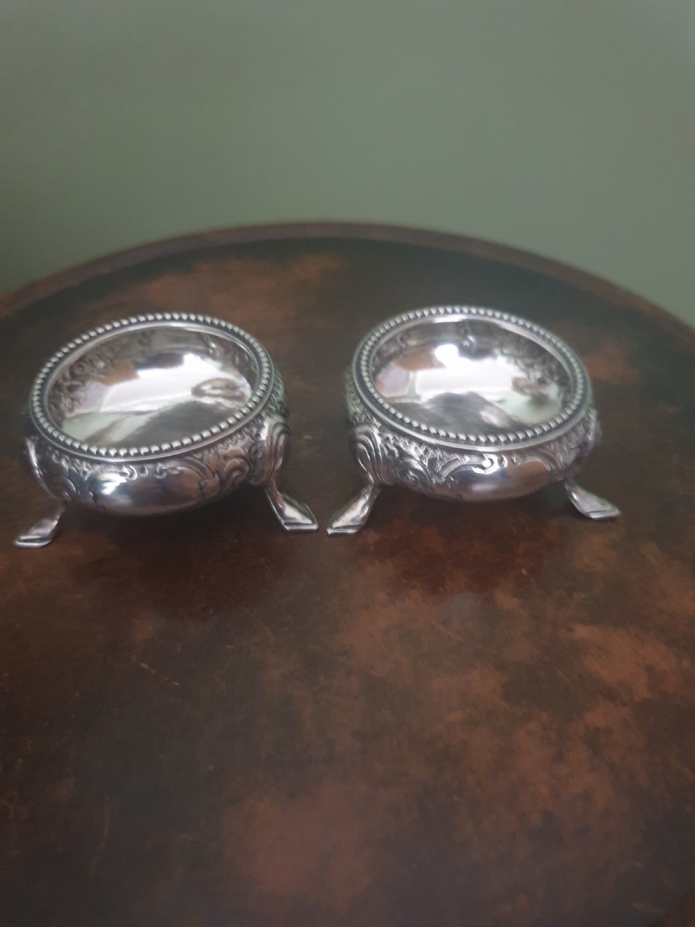 A pair of Victorian sterling silver open salt cellars with embossed floral patterns, beaded rims, and three pad feet.