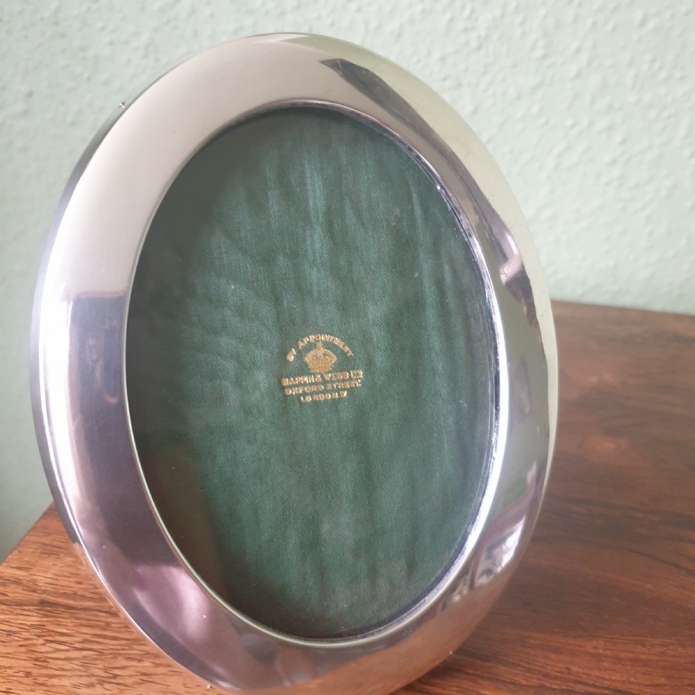 An oval sterling silver photograph frame with a smooth polished finish and dark green fabric lining inside.