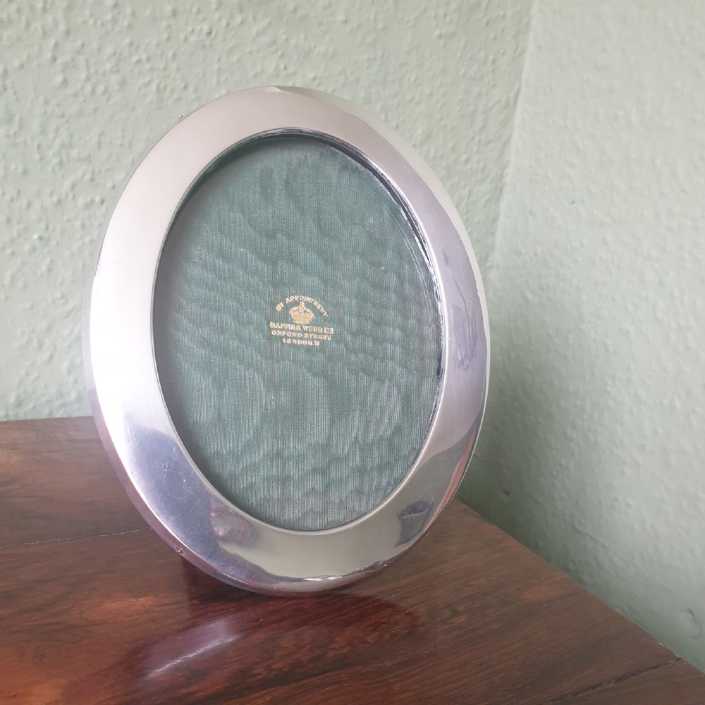 An oval sterling silver photograph frame with a smooth polished finish and dark green fabric lining inside. View V