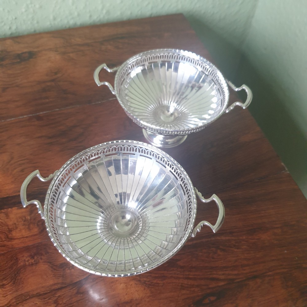 A pair of sterling silver tazzas featuring fluted bowls, pierced geometric rims, twin handles, and circular pedestal feet.