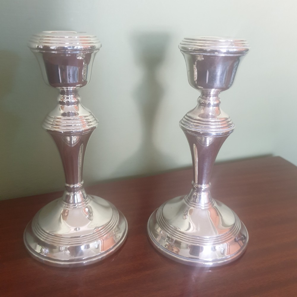 A pair of hallmarked sterling silver candlesticks featuring stepped circular bases, baluster stems, and flared nozzles on a dark wood surface.