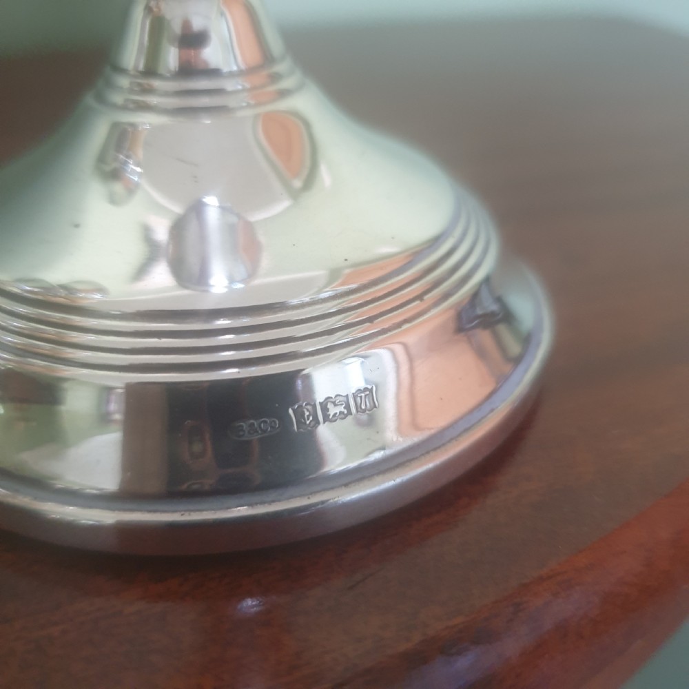 A pair of hallmarked sterling silver candlesticks featuring stepped circular bases, baluster stems, and flared nozzles on a dark wood surface. View II