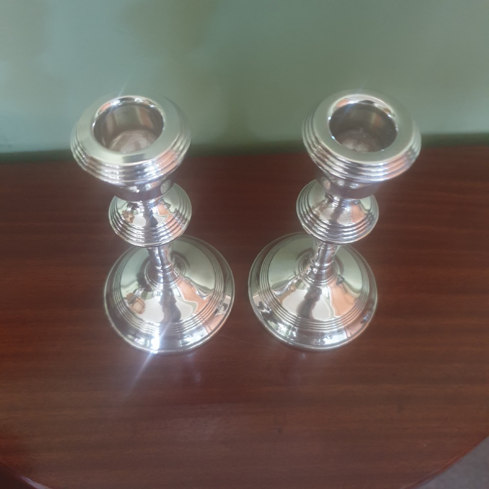 A pair of hallmarked sterling silver candlesticks featuring stepped circular bases, baluster stems, and flared nozzles on a dark wood surface. View III