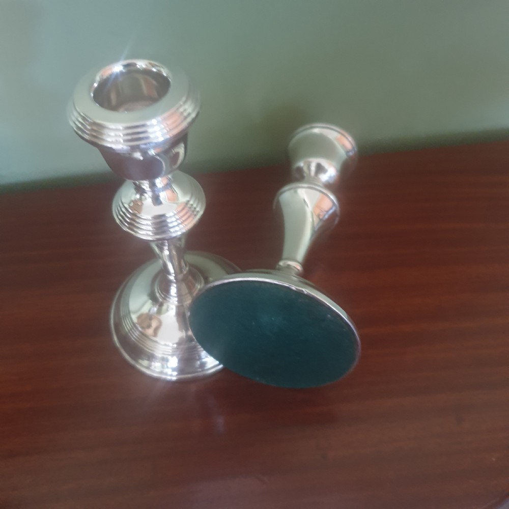 A pair of hallmarked sterling silver candlesticks featuring stepped circular bases, baluster stems, and flared nozzles on a dark wood surface. View IV