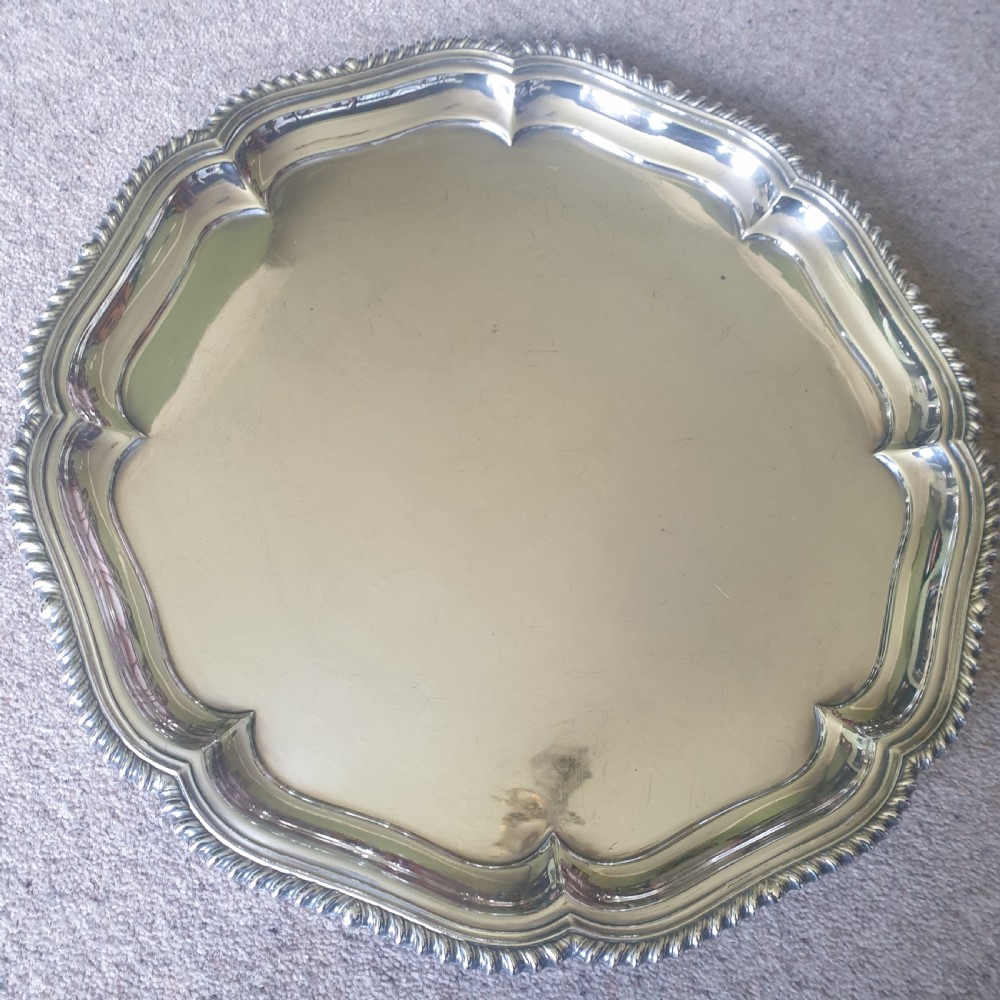 A circular silver-plated salver featuring a shaped, contoured border with gadrooned edge detailing.