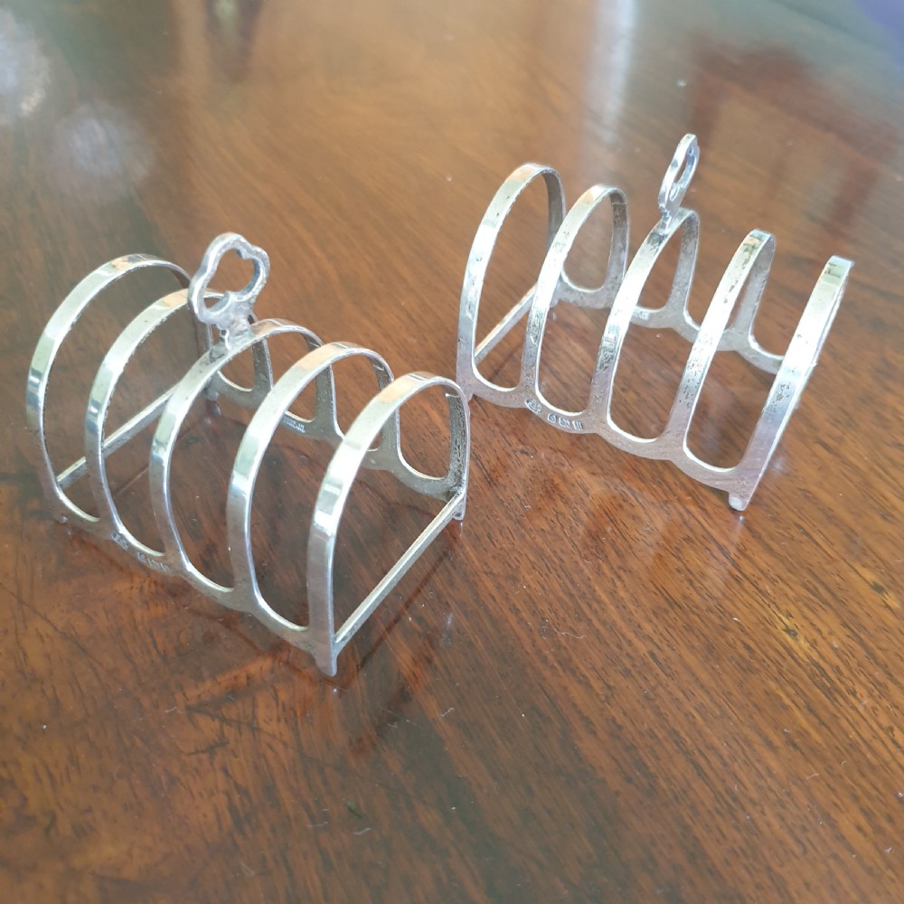 A pair of four-slot sterling silver toast racks featuring curved arches and trefoil central handles resting on a polished wooden surface. View II