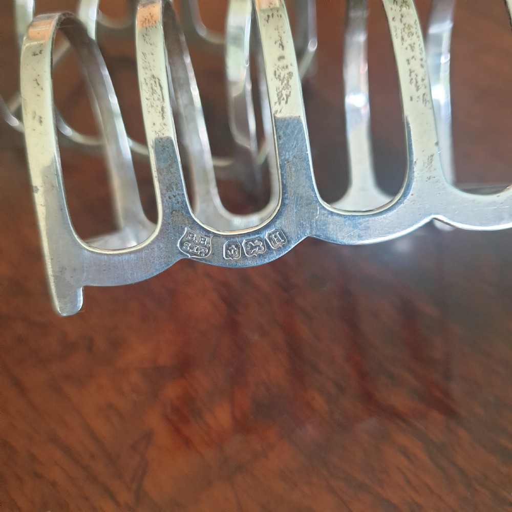 A pair of four-slot sterling silver toast racks featuring curved arches and trefoil central handles resting on a polished wooden surface. View III