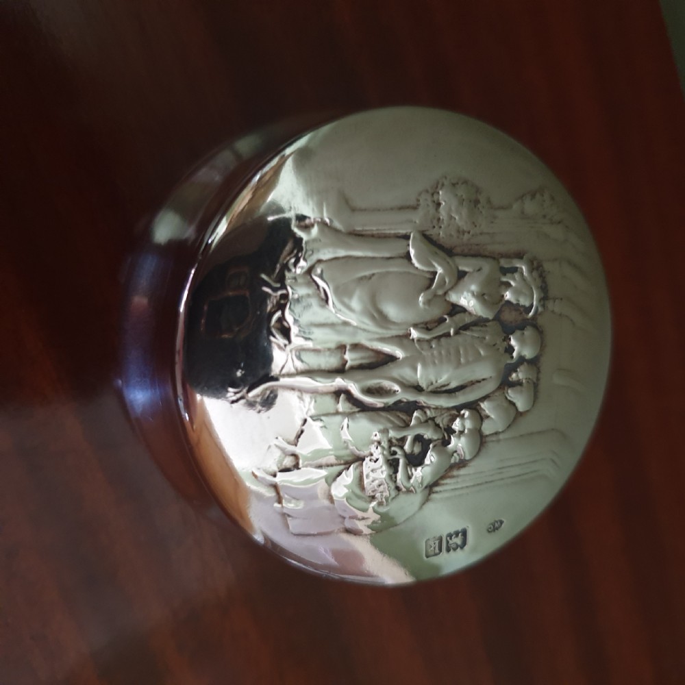 A circular Edwardian sterling silver pot lid featuring embossed figures and official London hallmarks.