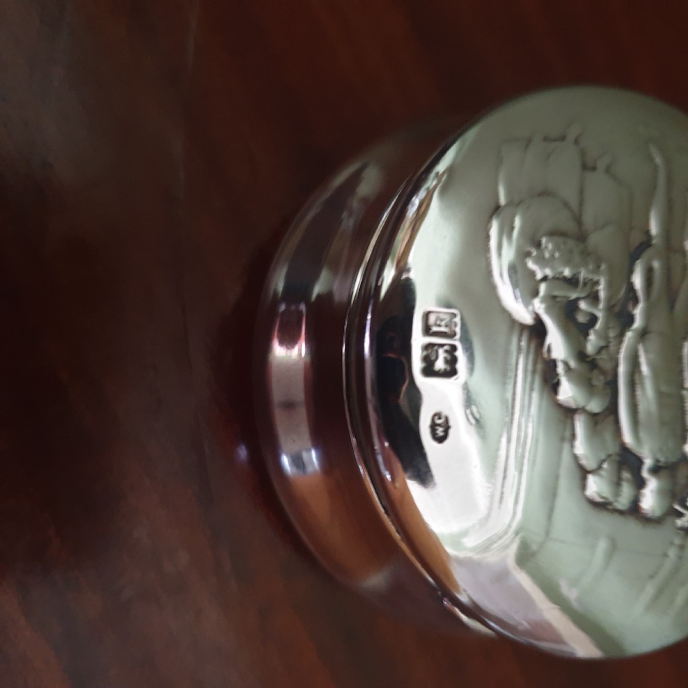 A circular Edwardian sterling silver pot lid featuring embossed figures and official London hallmarks. View II