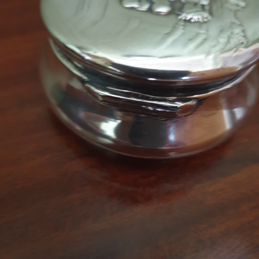 A circular Edwardian sterling silver pot lid featuring embossed figures and official London hallmarks. View IV
