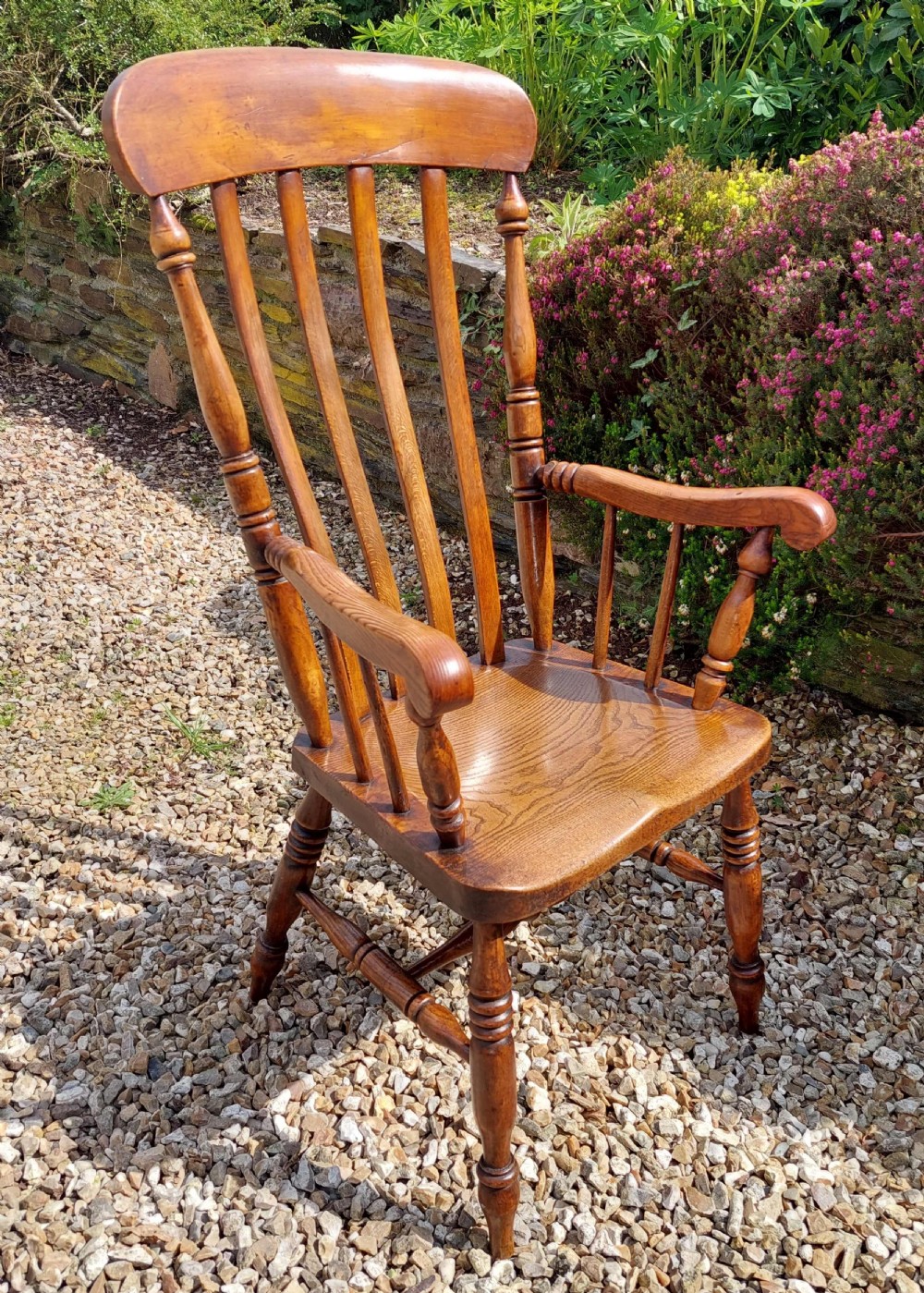 A 19th-century wooden lath back Windsor armchair with turned legs, curved armrests, and a contoured solid wood seat.