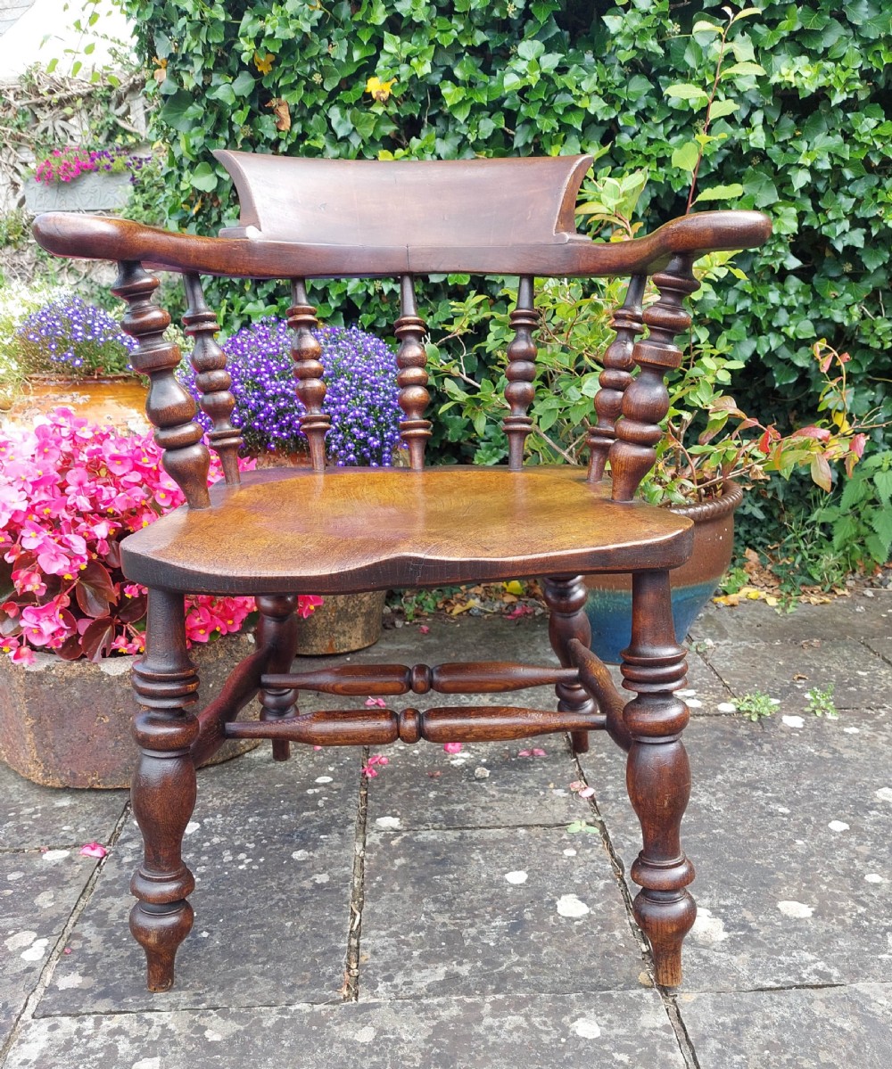 A dark brown antique smokers bow wooden armchair featuring turned spindles, a contoured elm saddle seat, and turned legs with stretchers. View II