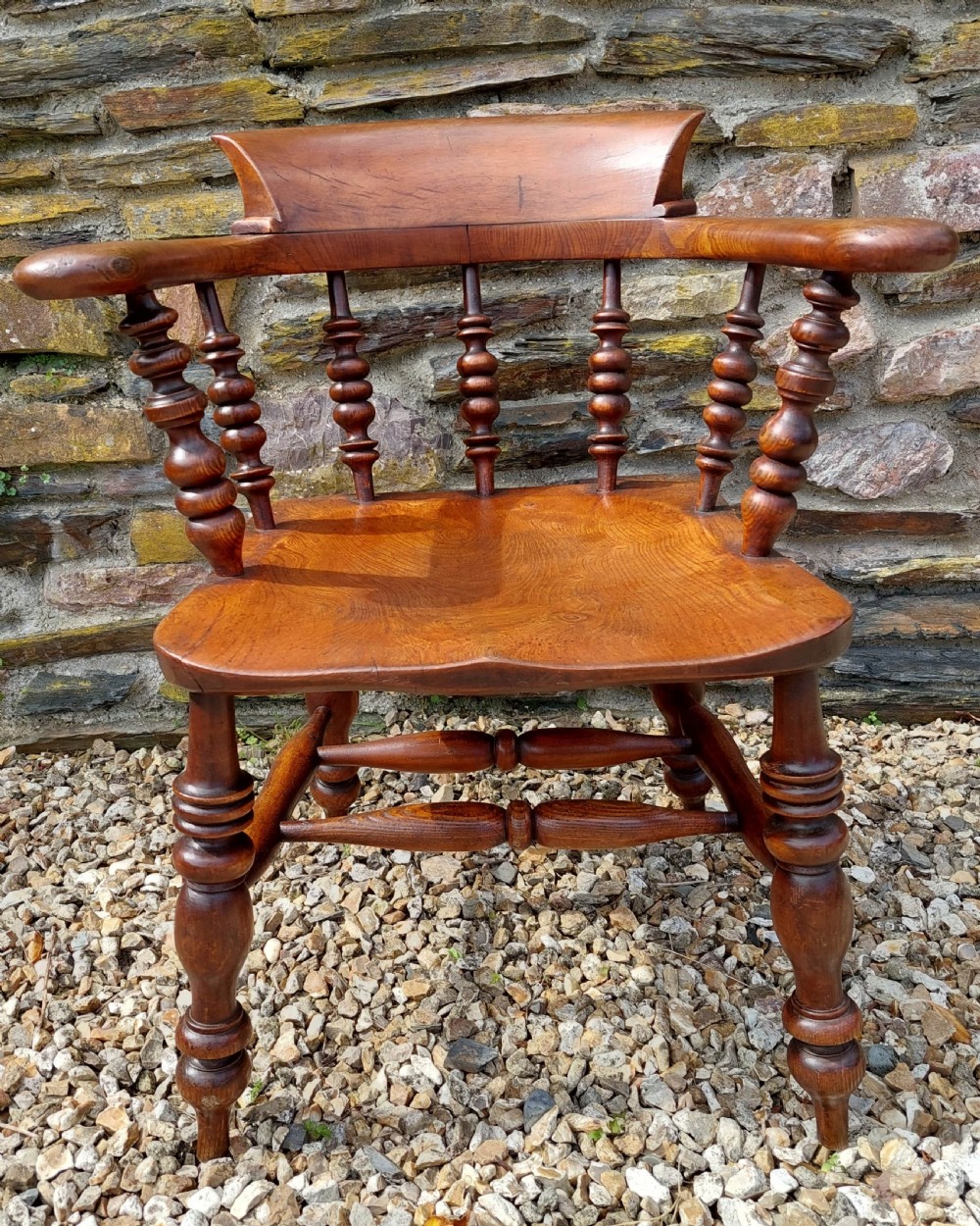 A 19th-century wooden smokers bow armchair featuring a curved crest rail, turned spindles, a shaped saddle seat, and turned legs with stretchers.