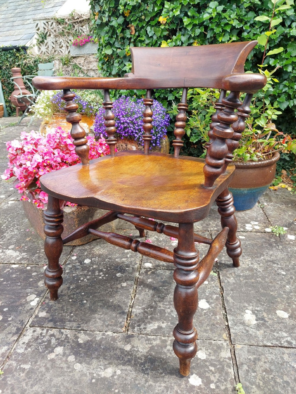 A dark brown antique smokers bow wooden armchair featuring turned spindles, a contoured elm saddle seat, and turned legs with stretchers.