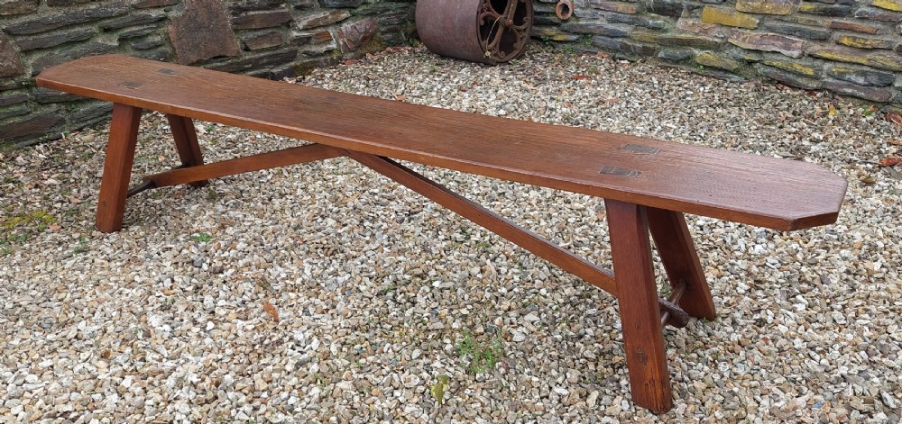 A long rustic pine bench with a flat timber top, splayed legs, and cross-braced support structure.