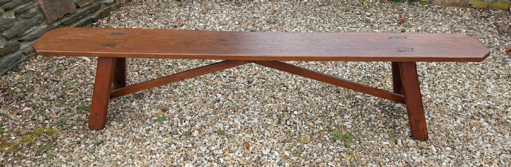 A long rustic pine bench with a flat timber top, splayed legs, and cross-braced support structure. View II