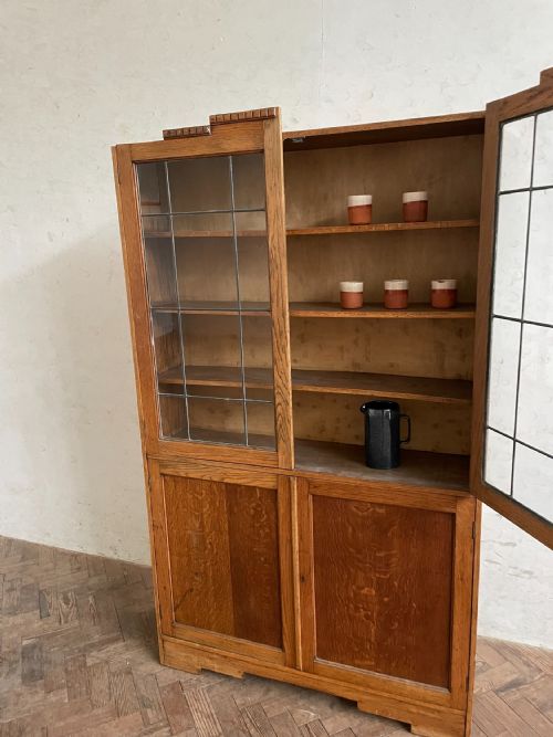 fig 1. An Art Deco oak cabinet featuring two upper leaded glass doors over two solid wood panel doors with a stepped top crest.