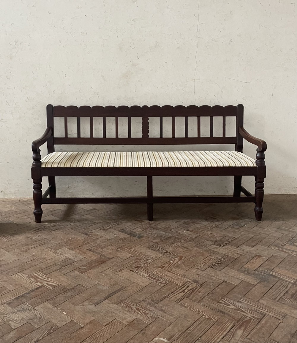A dark wood hallway bench featuring a scalloped top rail, a slatted backrest, turned legs, and a striped fabric seat cushion.