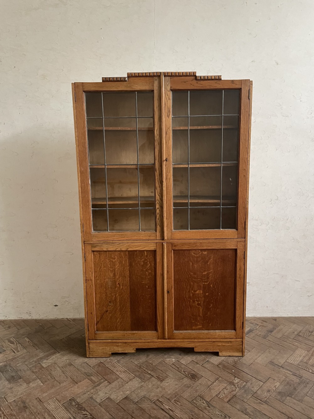 An Art Deco oak cabinet featuring two upper leaded glass doors over two solid wood panel doors with a stepped top crest.