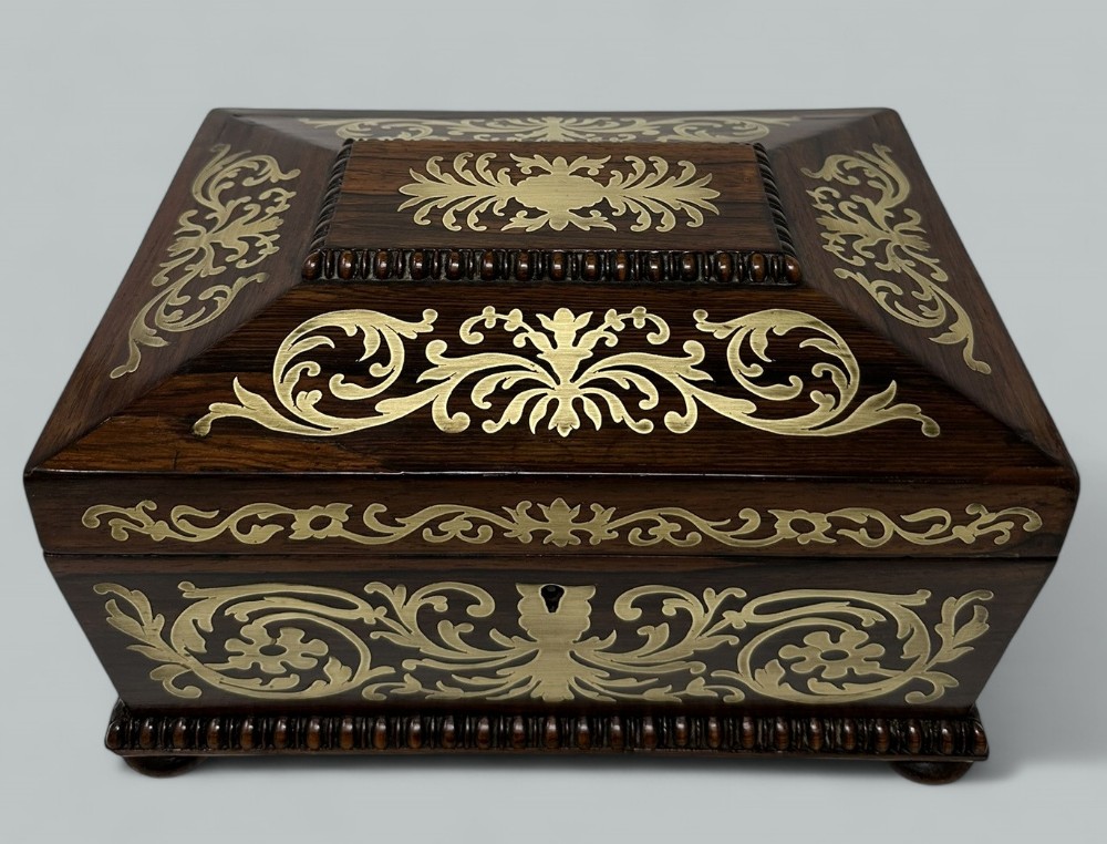 An antique dark rosewood rectangular casket featuring detailed brass scrollwork inlay and gadrooned wood edging.