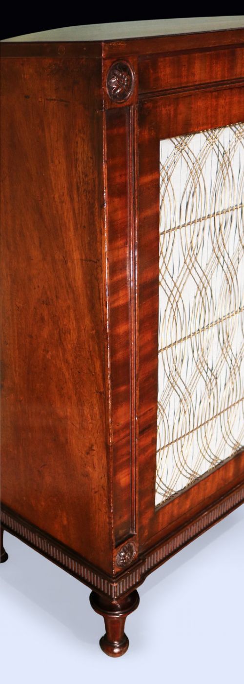 A Regency period two-door mahogany side cabinet featuring brass wire grille panels lined with pleated fabric and raised on turned legs. View III