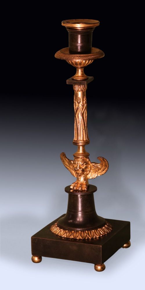 A pair of 19th-century French Empire style candlesticks featuring patinated bronze columns supported by gilded ormolu winged lions on square bases. View II