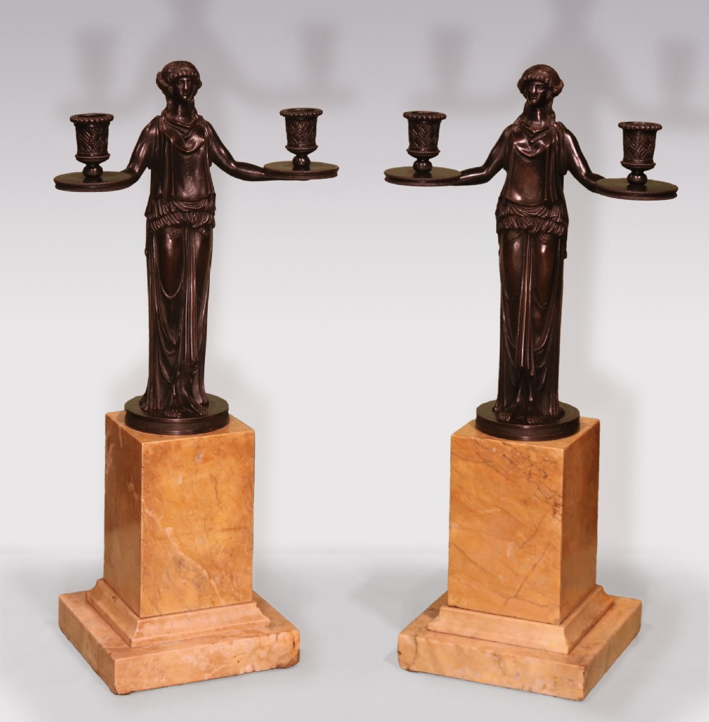 A pair of patinated bronze female caryatid candelabra holding two sconces each, mounted on tall rectangular yellow marble bases.