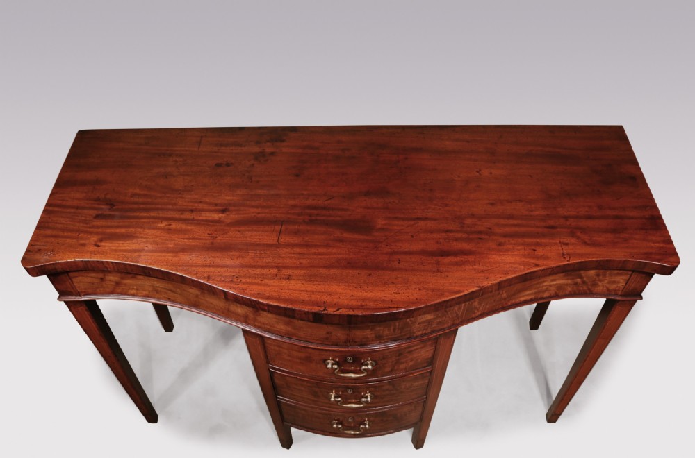 A George III period mahogany serving table featuring a curved front, central drawer stack with brass swan-neck handles, and tapered square legs. View III