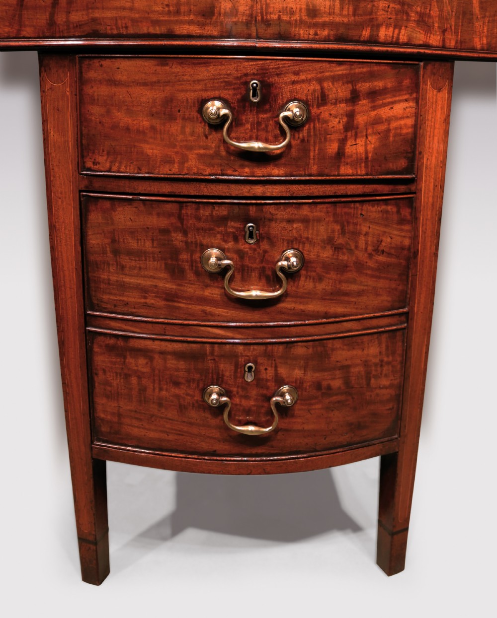 A George III period mahogany serving table featuring a curved front, central drawer stack with brass swan-neck handles, and tapered square legs. View IV
