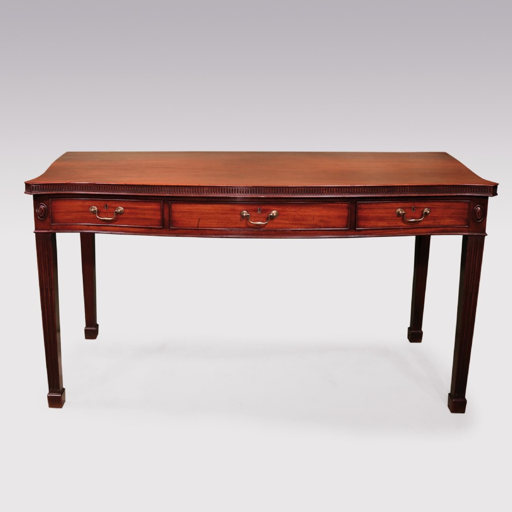 An 18th-century George III mahogany serving table featuring a serpentine front, three drawers with brass swan-neck handles, and fluted square tapered legs.